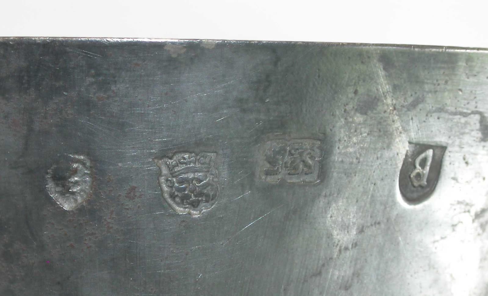 A row of small worn marks punched into the rim of an old silver cup